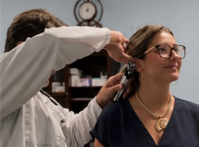 A clinician examining a woman's ear with an otoscope